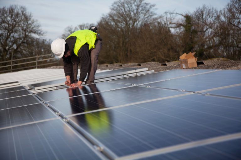 Technician in hi-vis and hard hat installing solar panels on a farm rooftop