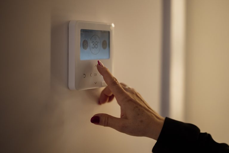 Engineer adjusting a home thermostat during a heating survey